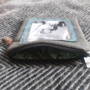 May include: A small gray zippered pouch with a black zipper. The pouch has a clear plastic window with a black and white photo inside. The pouch is lined with a blue and black paisley fabric.