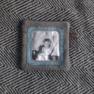 May include: A gray zippered pouch with a blue and white photo of a young girl blowing out candles on a birthday cake. The photo is framed with a blue border and the pouch has a small black tag with the text "Jackie" on it.