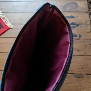 Peut inclure: Une pochette zipp&eacute;e turquoise avec une doublure bordeaux. La pochette est ouverte et la doublure est visible.