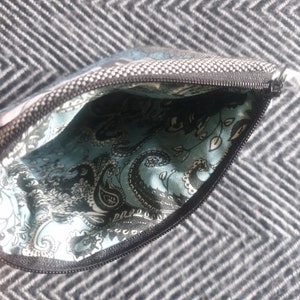 May include: A small zippered pouch with a black and white paisley pattern lining. The pouch is made of a gray fabric with a white polka dot pattern.