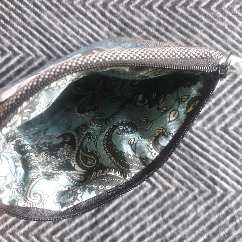 May include: A small zippered pouch with a black and white paisley pattern lining. The pouch is made of a gray fabric with a white polka dot pattern.