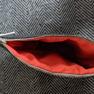 Puede incluir: Una bolsa de cremallera de denim negro con forro rojo. La bolsa est&aacute; abierta y la cremallera es visible.