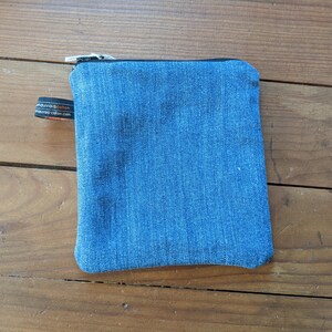 May include: A small blue denim zippered pouch with a black zipper pull and a black label with white text.