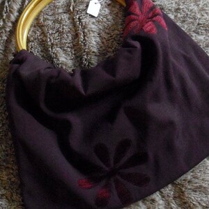 以下が含まれることがあります： 木製の輪っかハンドルと赤い刺繍の花柄が施された、濃い茶色の布製のトートバッグです。