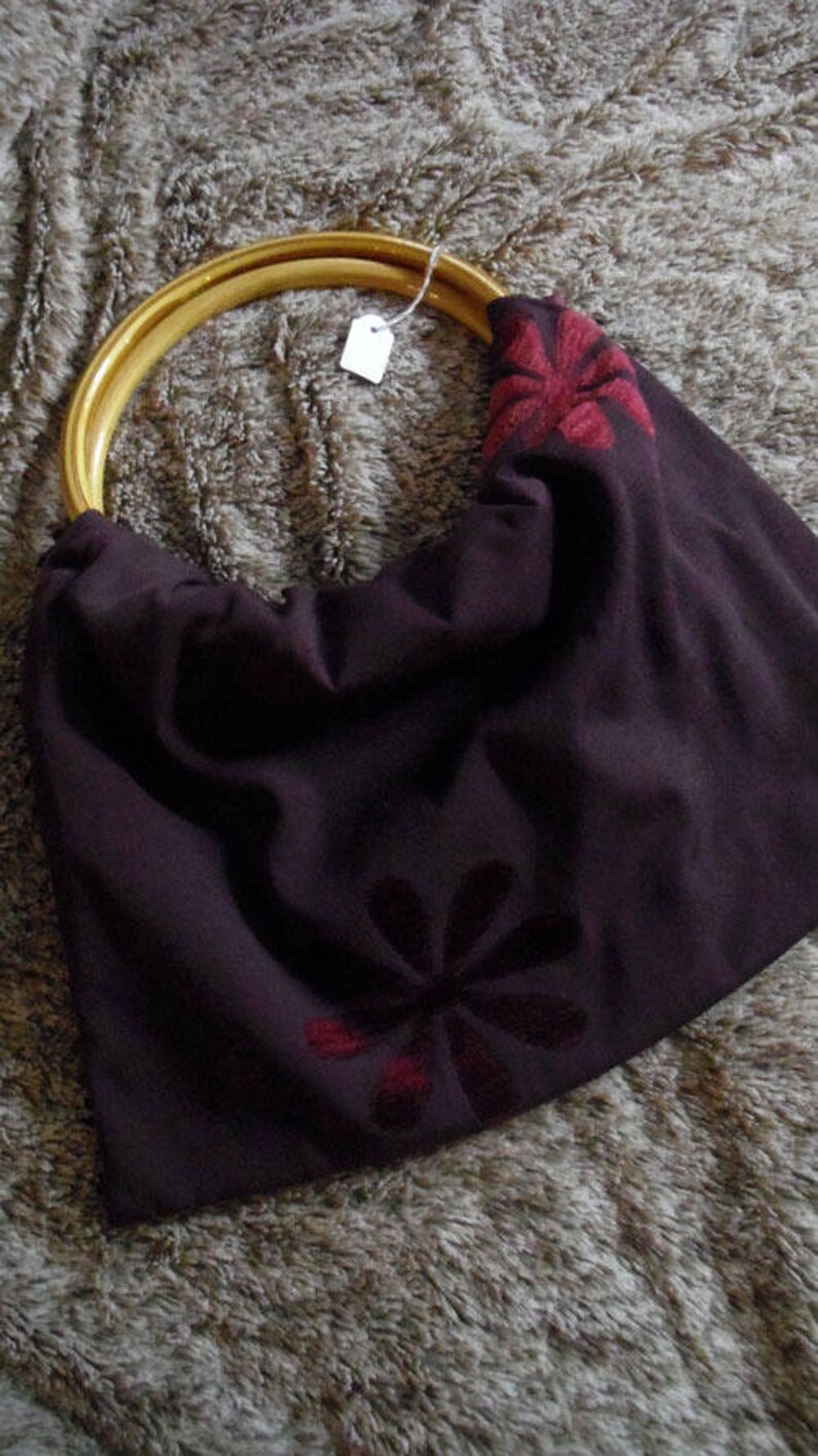 以下が含まれることがあります： 木製の輪っかハンドルと赤い刺繍の花柄が施された、濃い茶色の布製のトートバッグです。
