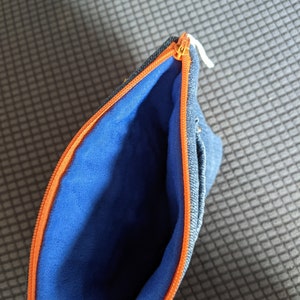 May include: A blue denim zippered pouch with an orange zipper and a blue fleece lining.