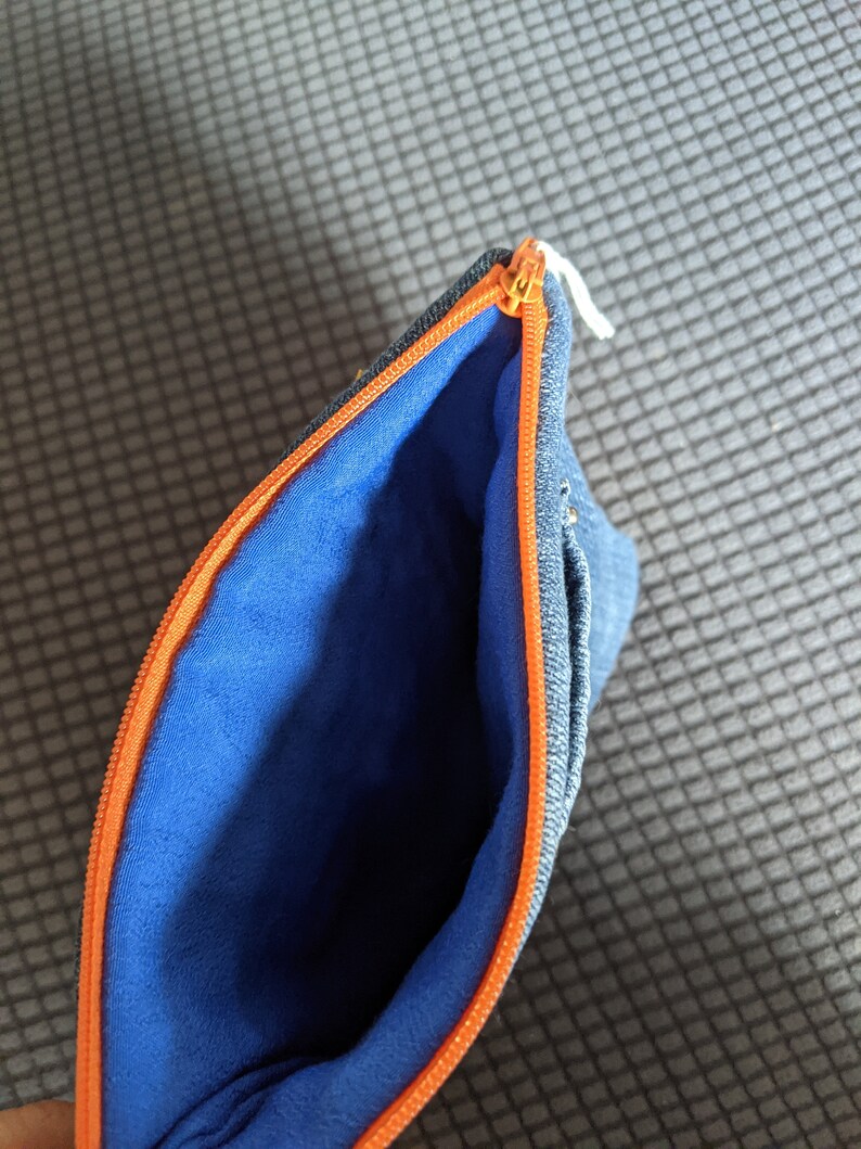 May include: A blue denim zippered pouch with an orange zipper and a blue fleece lining.