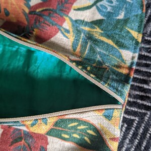 Pu&ograve; includere: Primo piano di una cerniera su una borsa in tessuto beige con una stampa a foglie tropicali in tonalit&agrave; di verde, giallo, rosso e blu.