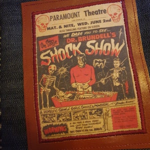 May include: A vintage-style poster for a horror show called "Dr. Brundell's Shock Show" at the Paramount Theatre. The poster features a skeleton, a monster, and a man in a tuxedo. The text on the poster reads "We dare you to see... Dr. Brundell's Shock Show. A horrific show of girls, ghouls & monsters.  Zombie Now!"
