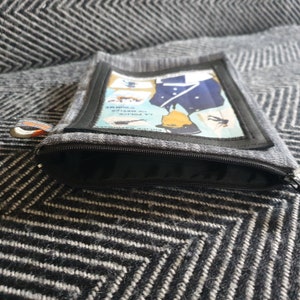 May include: A gray zippered pouch with a black zipper. The pouch has a rectangular patch with a vintage illustration of a police officer in uniform. The text on the patch reads "LA POLICE" and "POLICE NATIONALE".