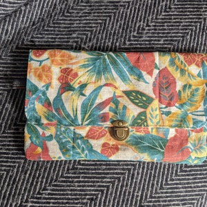 Pu&ograve; includere: Una piccola pochette rettangolare con stampa floreale. Il tessuto &egrave; di colore beige chiaro con motivi floreali rossi, gialli e verdi. La pochette &egrave; dotata di una chiusura a scatto in ottone.