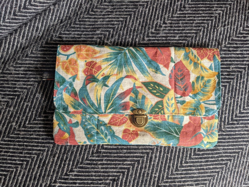 Pu&ograve; includere: Una piccola pochette rettangolare con stampa floreale. Il tessuto &egrave; di colore beige chiaro con motivi floreali rossi, gialli e verdi. La pochette &egrave; dotata di una chiusura a scatto in ottone.