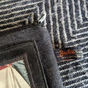 May include: Black zippered pouch with a black suede patch and a colorful fabric design. The pouch has a label that reads "Jackie fileu www.jackie-fileu.com".