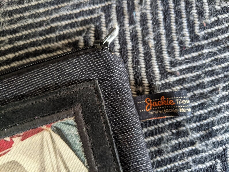May include: Black zippered pouch with a black suede patch and a colorful fabric design. The pouch has a label that reads "Jackie fileu www.jackie-fileu.com".