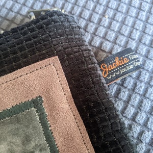 May include: A black, green, and pink fabric pouch with a stitched border. The pouch has a label that reads "Jackie filer www.jackie-filer.com".