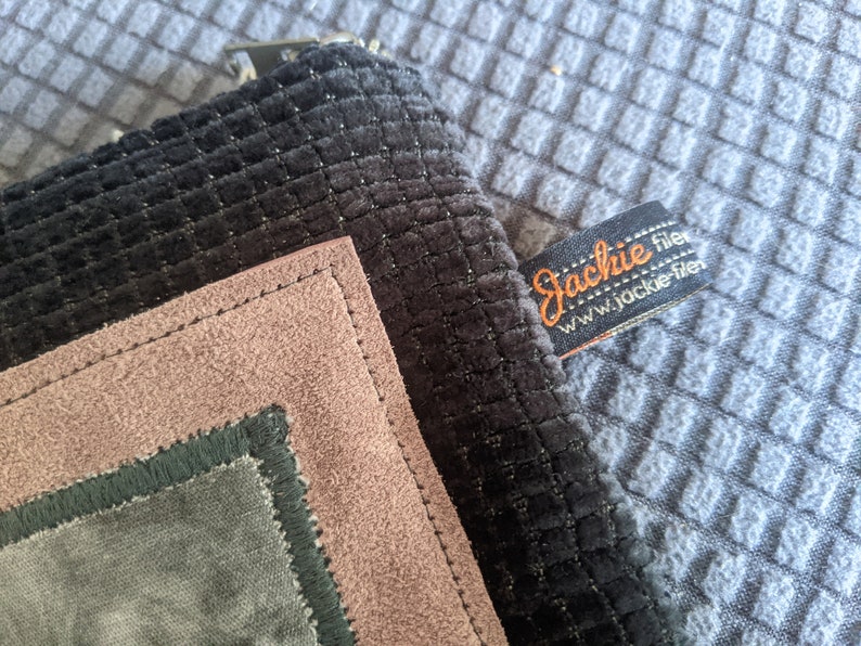 May include: A black, green, and pink fabric pouch with a stitched border. The pouch has a label that reads "Jackie filer www.jackie-filer.com".