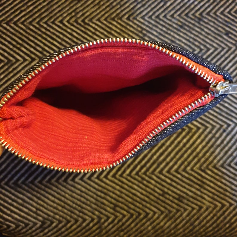 May include: A black zippered pouch with a red fabric lining. The pouch is open and the zipper is visible.