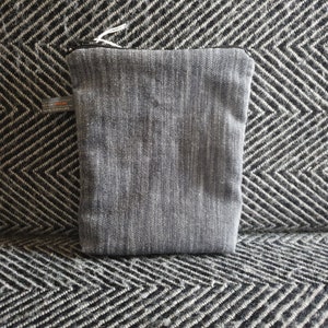 May include: A gray zippered pouch with a subtle striped pattern. The pouch is made of a soft, textured fabric.