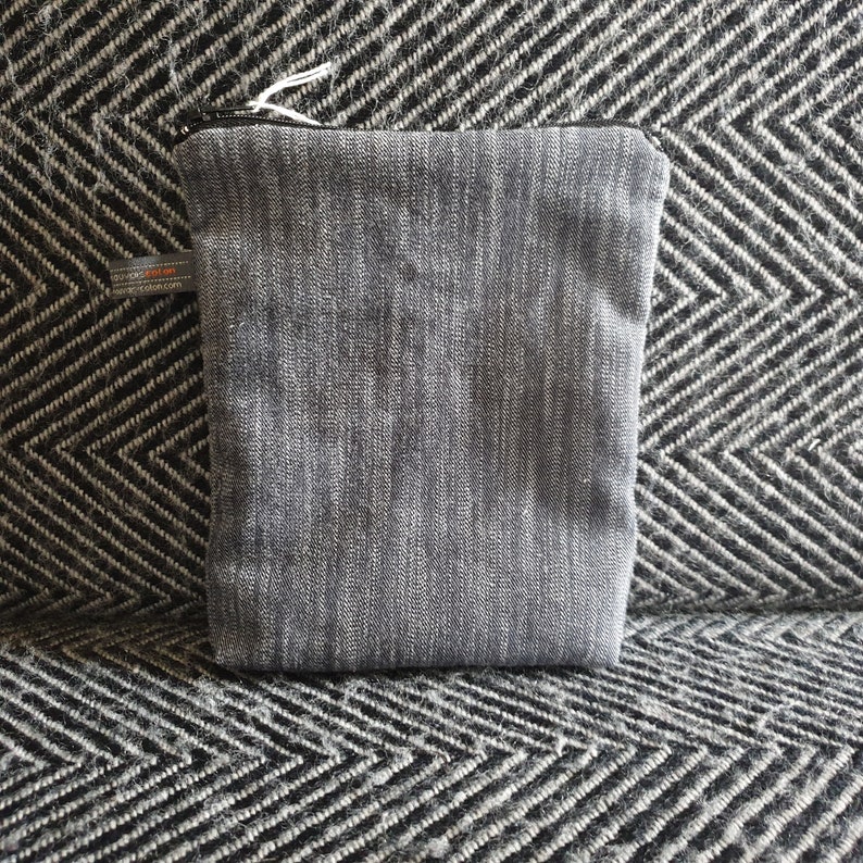 May include: A gray zippered pouch with a subtle striped pattern. The pouch is made of a soft, textured fabric.