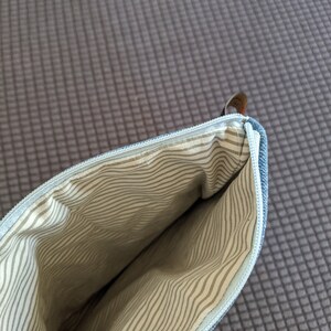Puede incluir: Una bolsa de cremallera de mezclilla azul con un forro a rayas blanco y gris. La bolsa est&aacute; abierta y el forro es visible.