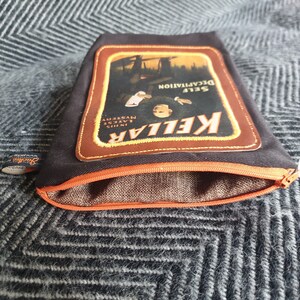 Pu&ograve; includere: Una pochette nera con cerniera e una toppa in pelle marrone con una pubblicit&agrave; vintage per "KELLAR, SELF DECAPITATION, IN THIS LATEST MYSTERY".