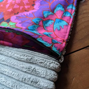 K&ouml;nnte beinhalten: Eine Rei&szlig;verschlusstasche mit einem bunten Blumenmusterstoff auf der oberen H&auml;lfte und einem grauen Cordstoff auf der unteren H&auml;lfte.