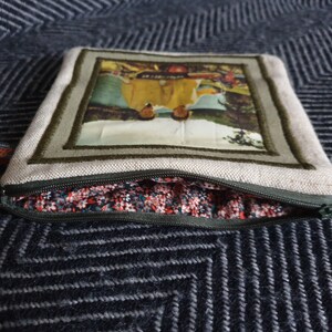 May include: A beige zippered pouch with a green zipper and a floral fabric lining. The pouch has a framed image of two people in a winter scene.
