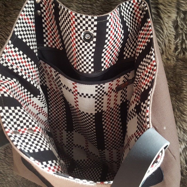 May include: A brown canvas tote bag with a black and white checkered lining. The bag has a zippered pocket on the inside and a black strap.