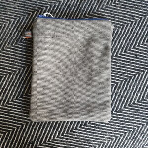 May include: A gray zippered pouch with a blue zipper pull. The pouch is made of a textured fabric and has a small orange and white label.