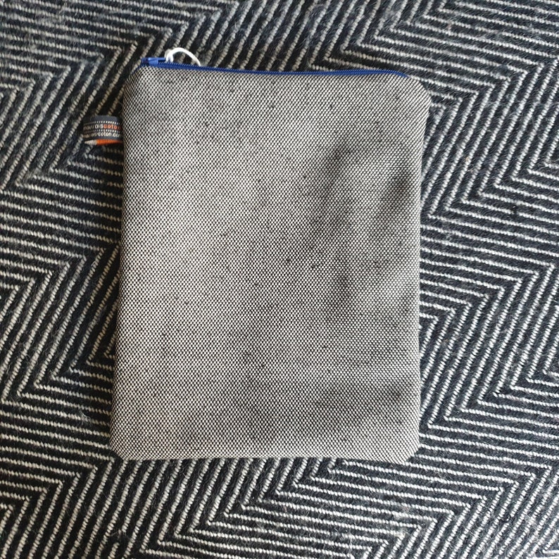 May include: A gray zippered pouch with a blue zipper pull. The pouch is made of a textured fabric and has a small orange and white label.