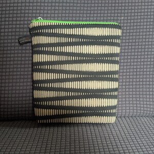 May include: A black and beige zippered pouch with a green zipper. The pouch has a repeating pattern of beige lines on a black background.