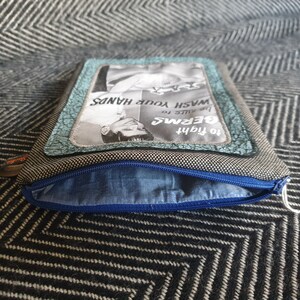 May include: A gray and black zippered pouch with a blue lining. The pouch has a vintage-style advertisement on the front that reads "To fight germs, be sure to wash your hands."