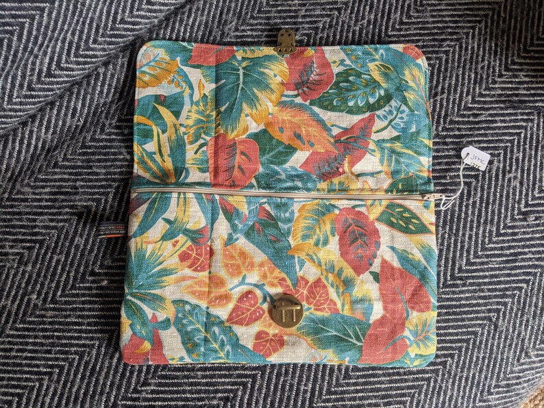 Pu&ograve; includere: Una pochette con zip con stampa floreale che presenta foglie rosse, gialle e blu su uno sfondo bianco. La pochette ha una zip dorata e due chiusure dorate.