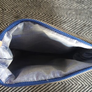May include: The inside of a small zippered pouch with a blue zipper and a light blue lining. The pouch is made of a black and white patterned fabric.