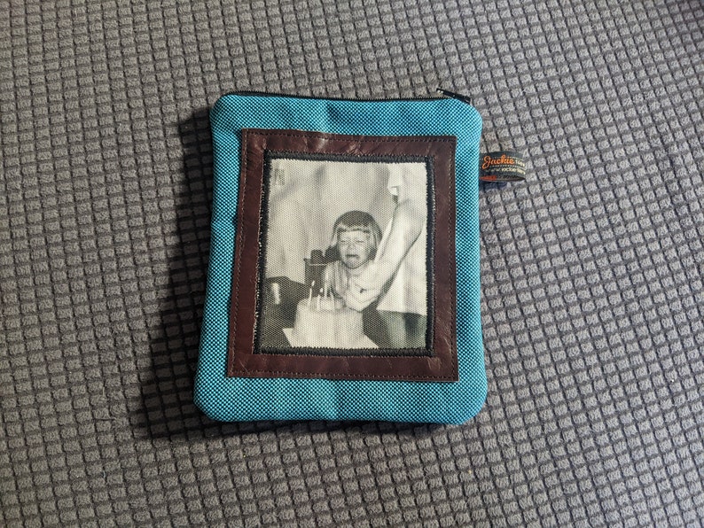 May include: A blue zippered pouch with a brown leather frame and a black and white photo of a young child blowing out candles on a birthday cake.