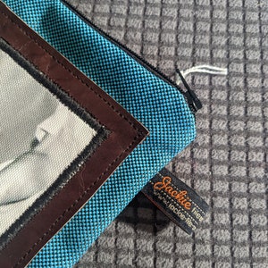 May include: A blue zippered pouch with a brown leather trim and a white and black photo insert. The pouch has a black tag that reads "Jackie tien" and "www.jackie-tien.com".