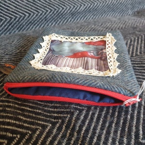 May include: A blue zippered pouch with a red zipper and a white lace frame around a printed image of a woman lying on a striped bed.