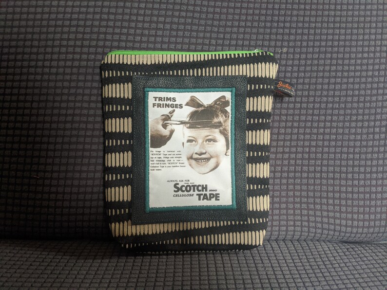 May include: A black and white zippered pouch with a green zipper pull. The pouch has a vintage advertisement for Scotch Cellulose Tape featuring a young girl with a bow in her hair. The ad text reads "Trims Fringes", "Scotch", and "Cellulose Tape".