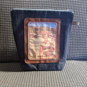 K&ouml;nnte beinhalten: Eine Rei&szlig;verschlusstasche aus Denim mit einem braunen Lederpatch, der ein Vintage-Foto einer Frau im Badeanzug am Strand zeigt.