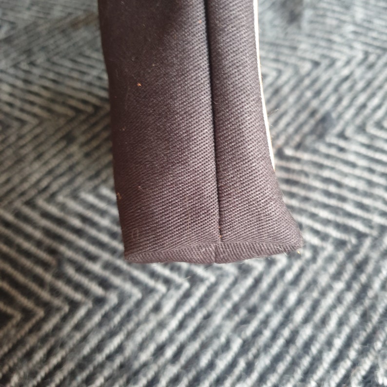 Pu&ograve; includere: Primo piano del bordo inferiore di una borsa di tela nera. Il tessuto &egrave; cucito con una cucitura dritta e ha una leggera lucentezza.