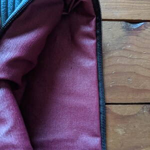 Peut inclure: Une pochette zipp&eacute;e bleu sarcelle avec une doublure bordeaux. La pochette est faite d'un tissu doux et textur&eacute;.
