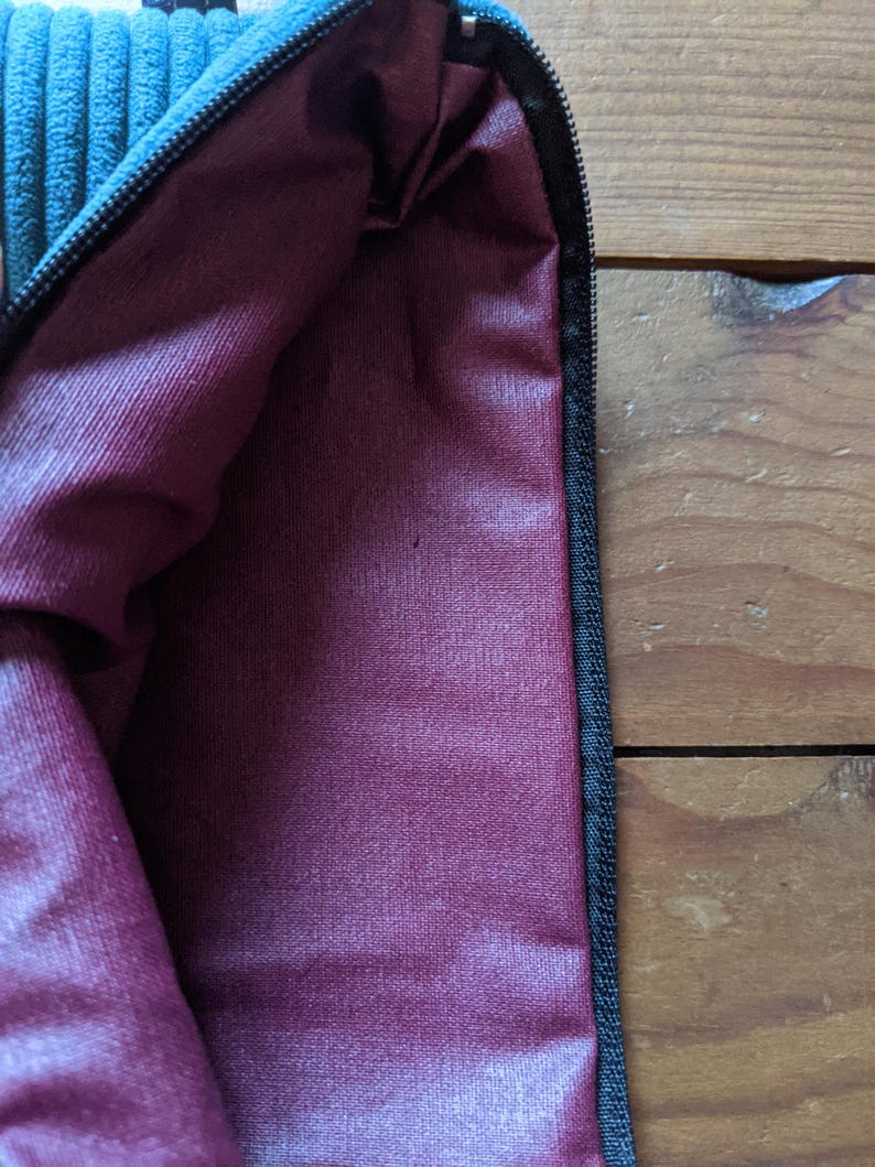 Peut inclure: Une pochette zipp&eacute;e bleu sarcelle avec une doublure bordeaux. La pochette est faite d'un tissu doux et textur&eacute;.