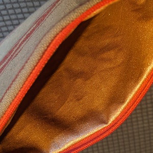 May include: A small, striped zippered pouch with a red zipper and a gold satin lining.