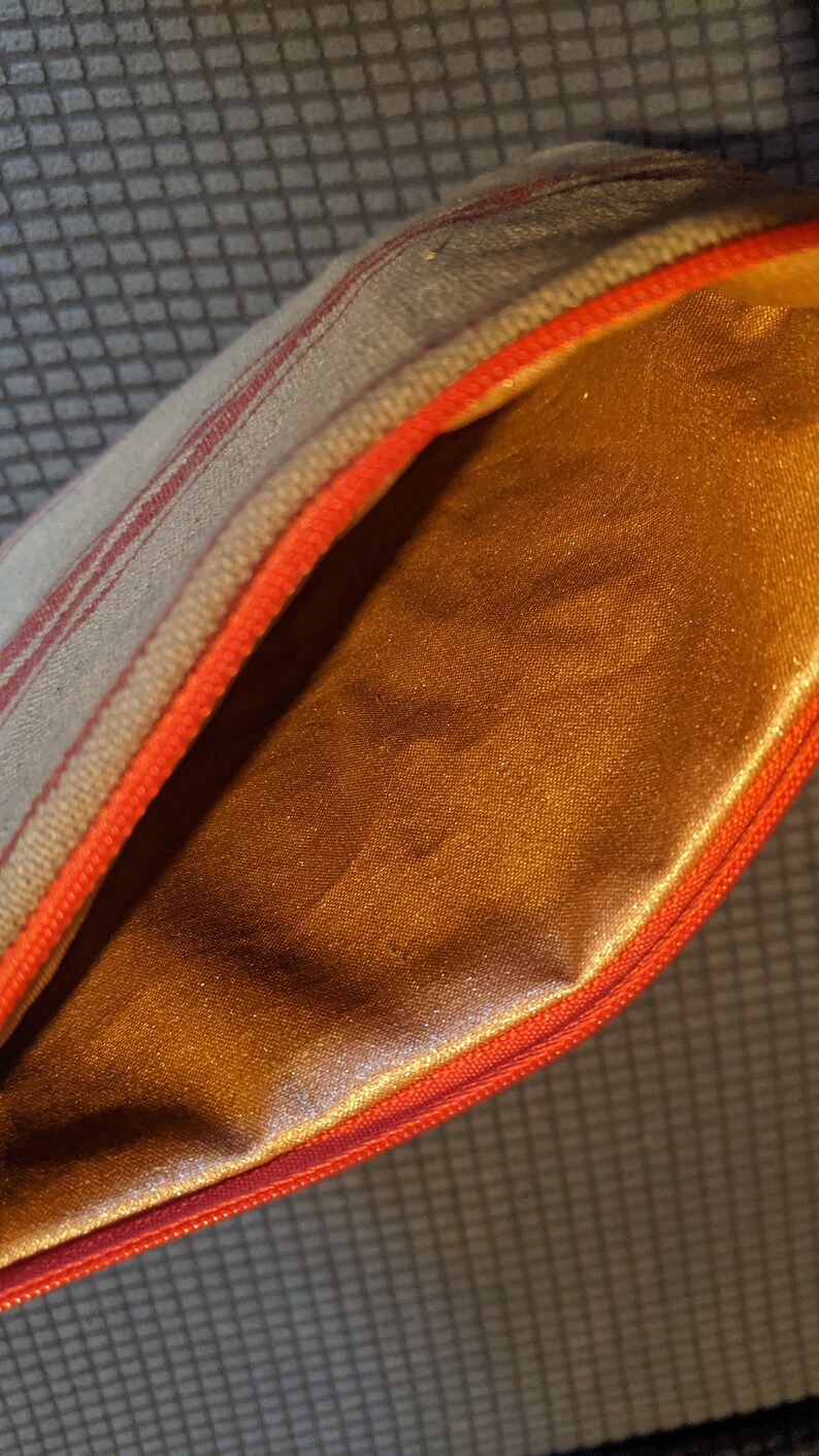 May include: A small, striped zippered pouch with a red zipper and a gold satin lining.