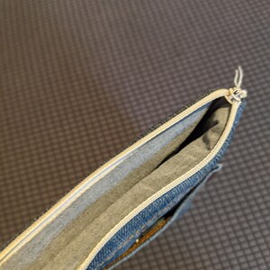 May include: A blue denim pencil case with a white zipper and a white lining. The case is open and the lining is visible.