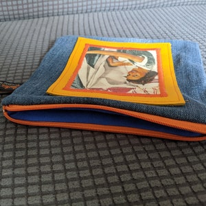 May include: A blue denim zippered pouch with a yellow frame around a vintage photo of a woman. The pouch has a blue zipper and an orange zipper pull.