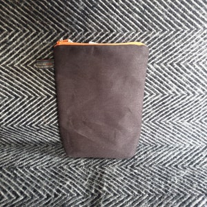 Pu&ograve; includere: Una pochette con cerniera marrone con una cerniera arancione. La pochette &egrave; realizzata in un tessuto morbido e testurizzato.