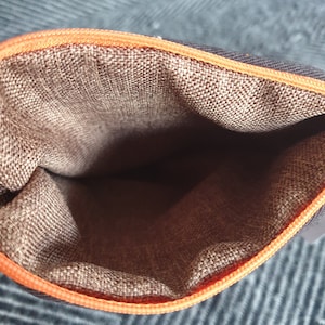 Pu&ograve; includere: L'interno di una pochette con cerniera marrone con una cerniera arancione. La pochette &egrave; realizzata in tessuto strutturato.