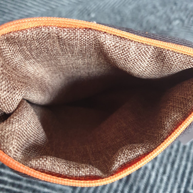 Pu&ograve; includere: L'interno di una pochette con cerniera marrone con una cerniera arancione. La pochette &egrave; realizzata in tessuto strutturato.