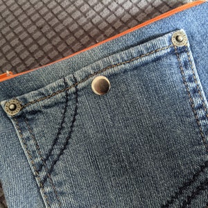 May include: A blue denim pouch with a large pocket and orange trim. The pouch has two silver metal rivets.